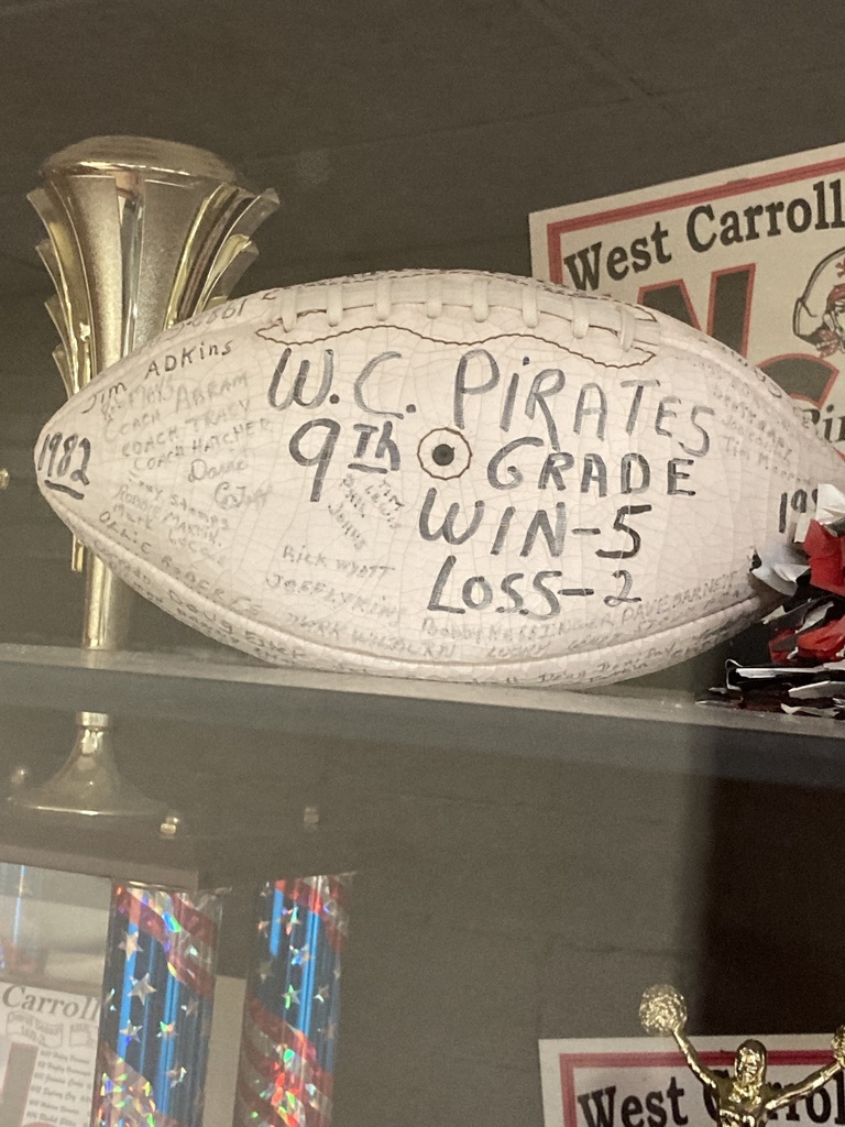Display case with a football labeled "W.C. Pirates 9th Grade Win-5 Loss-2" and a trophy.