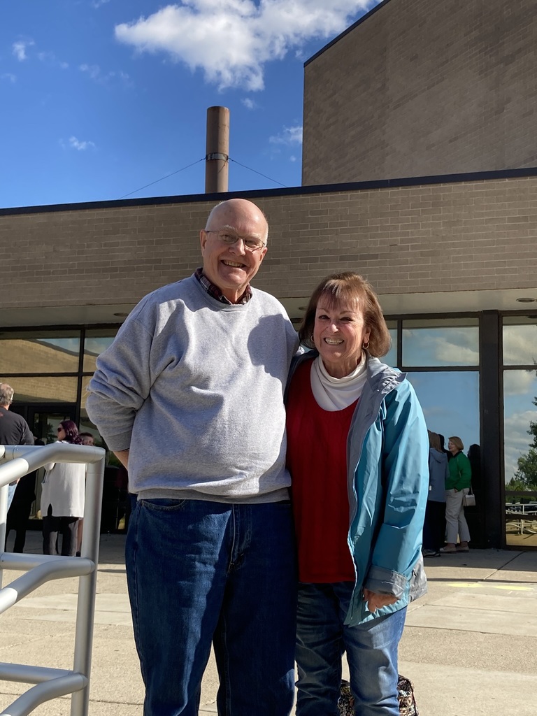 A man and a woman are smiling and standing next to each other in front of a building.
