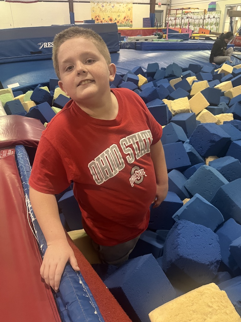 A child in a red t-shirt stands in a gym with blue and yellow foam blocks.