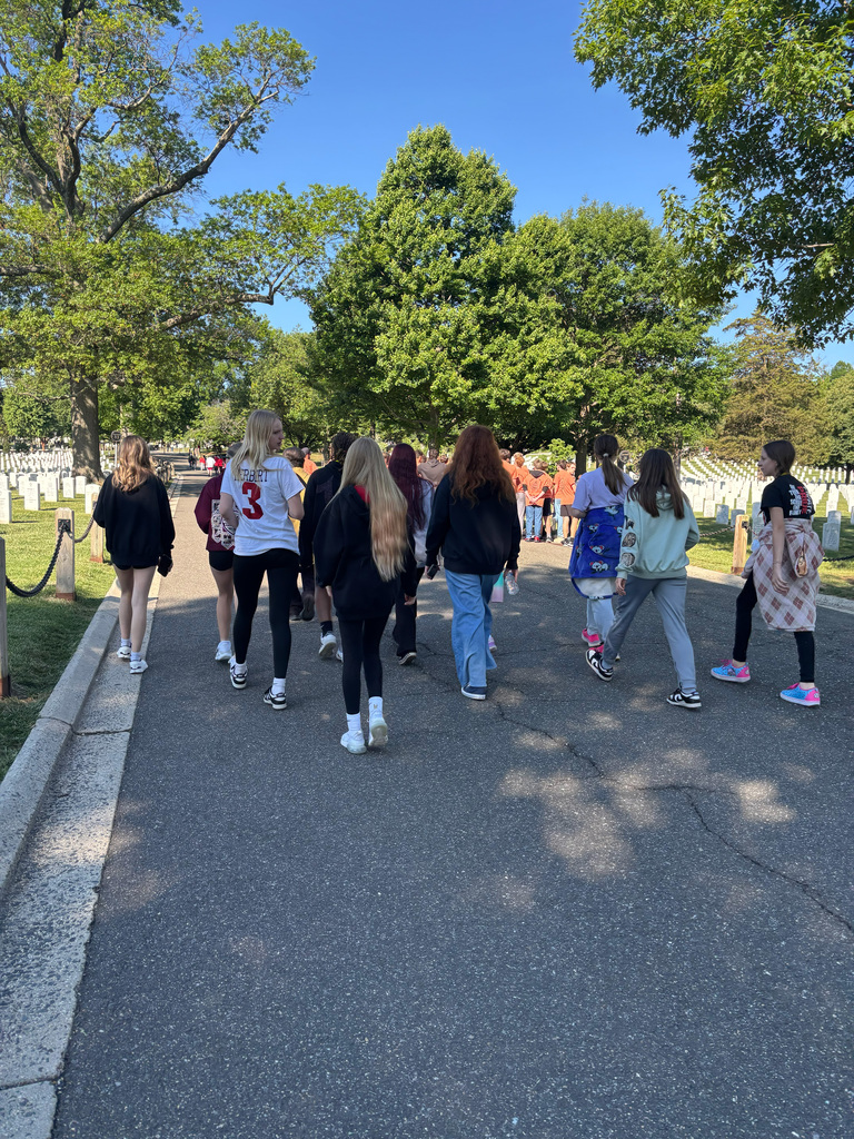 A group of individuals in casual clothing walks on a road with a cemetery in the background.