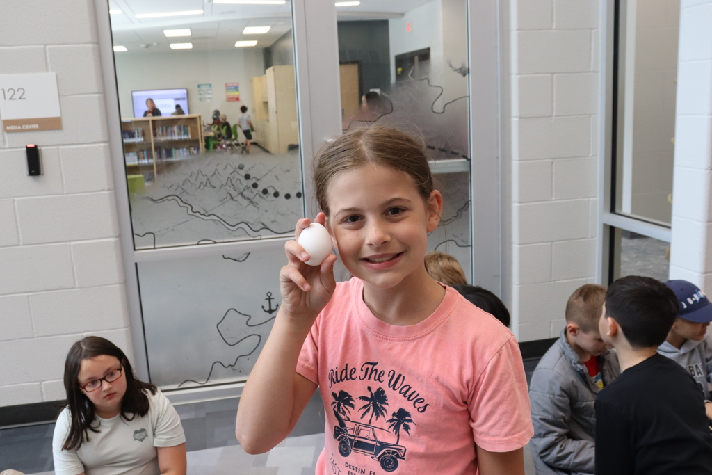 Girl in pink shirt holds a white egg in with children sitting on the floor.