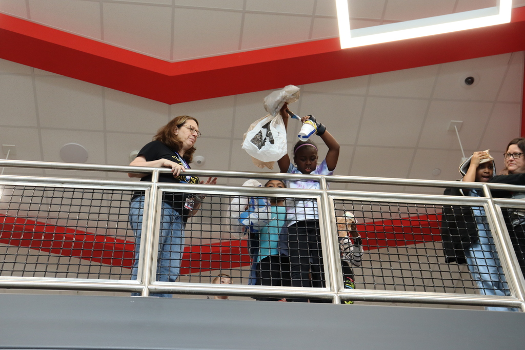 People on an upper level of a multi-story building, one of whom holds up a white bag.