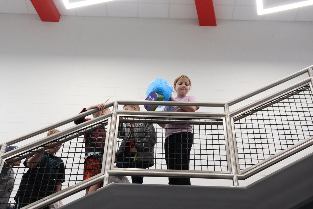 Several children in various clothes on a staircase, one holding a blue bag. The stairs have a metal railing.