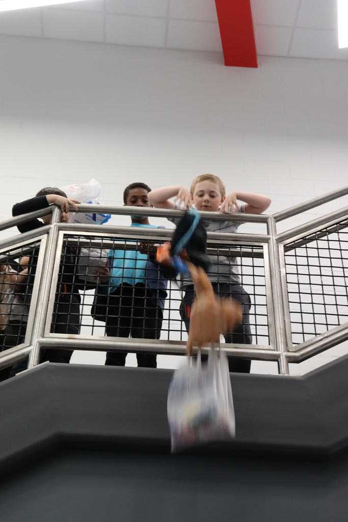 Four kids are standing on a staircase with metal railings. A brown object falls from above.