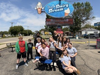 A group of children pose for a picture in front of an ice cream shop sign.
