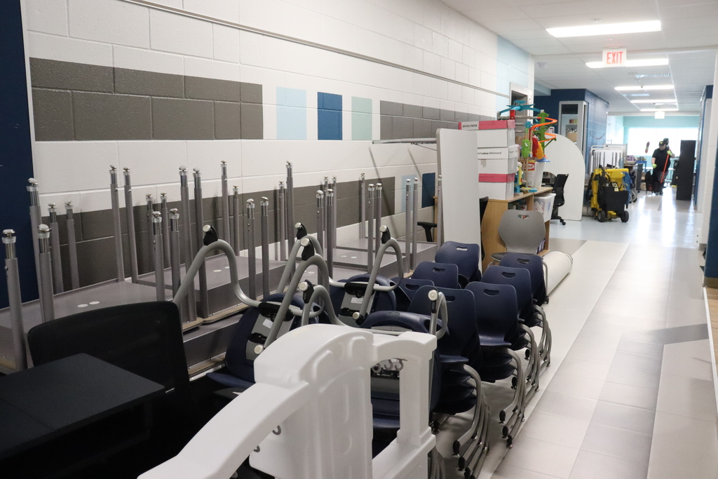 Hallway with blue chairs and tables stacked. Walls have gray and blue tiles.
