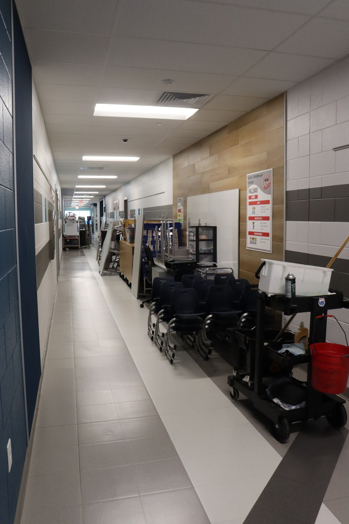 Hallway with tiled floor. White and blue walls on the left. Wooden wall on the right. Carts, bags, and a red bucket.