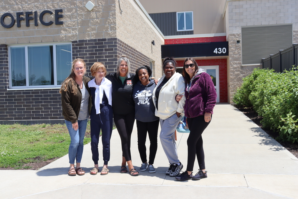 Six people pose in front of an office building. Two are wearing glasses, and two wear sneakers.