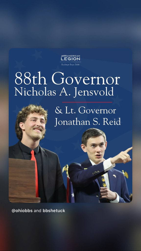 Two men, one in a red tie and one in a blue suit, standing behind a podium with blue background.