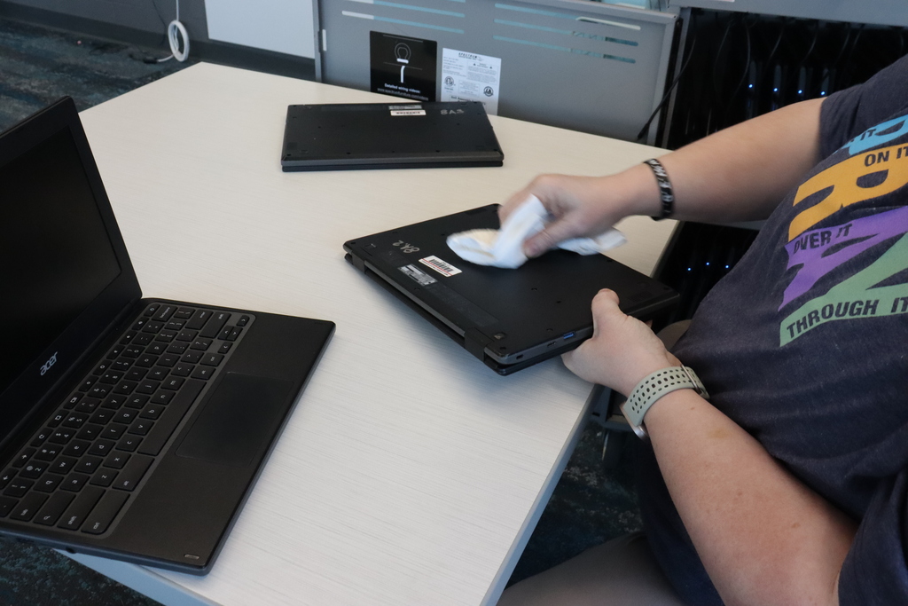 Person cleaning a laptop with a cloth. Another laptop is on the table.