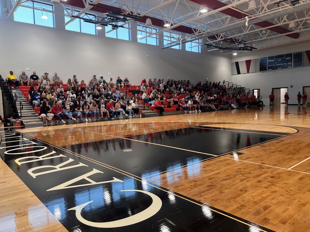 An indoor basketball court with the word "ORLANDO" on it. Spectators sit on benches in rows on the left side.