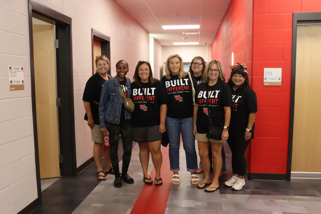 A group of people wearing matching shirts stand in a hallway with red walls and gray floors.