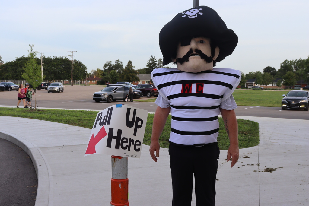 Person in a pirate costume stands beside a sign with an arrow, on a sidewalk.