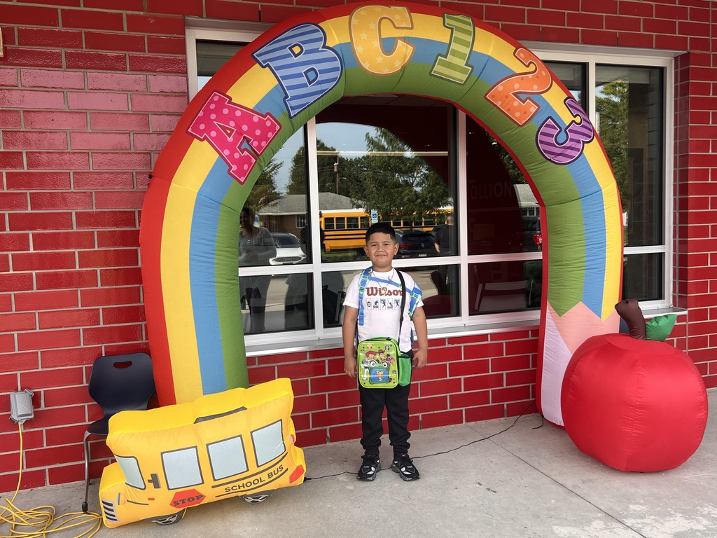 A young boy stands in front of a colorful archway in front of a brick building.
