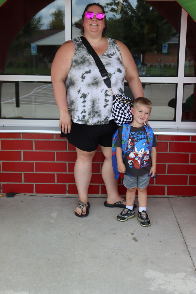 A woman and a young child stand outside a building with a red brick wall and a glass window.