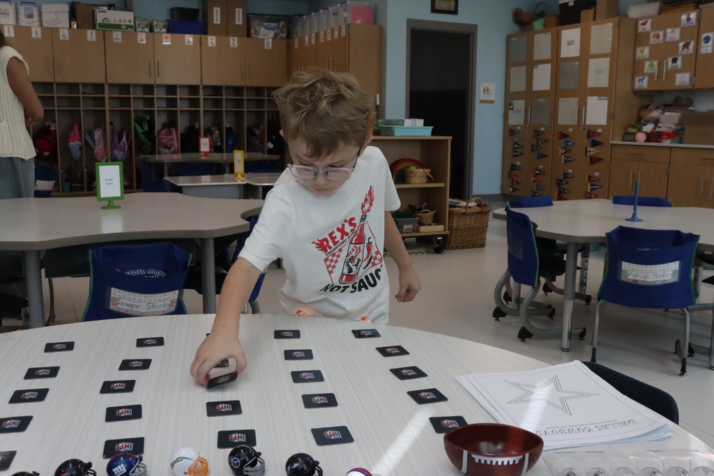 A boy wearing glasses and a white shirt plays a game with miniature footballs on a table.