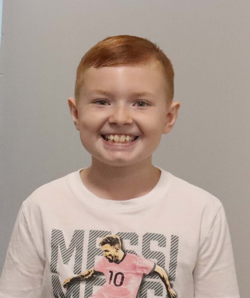 A child with red hair wearing a white shirt with a soccer player image and the text "MESSI".