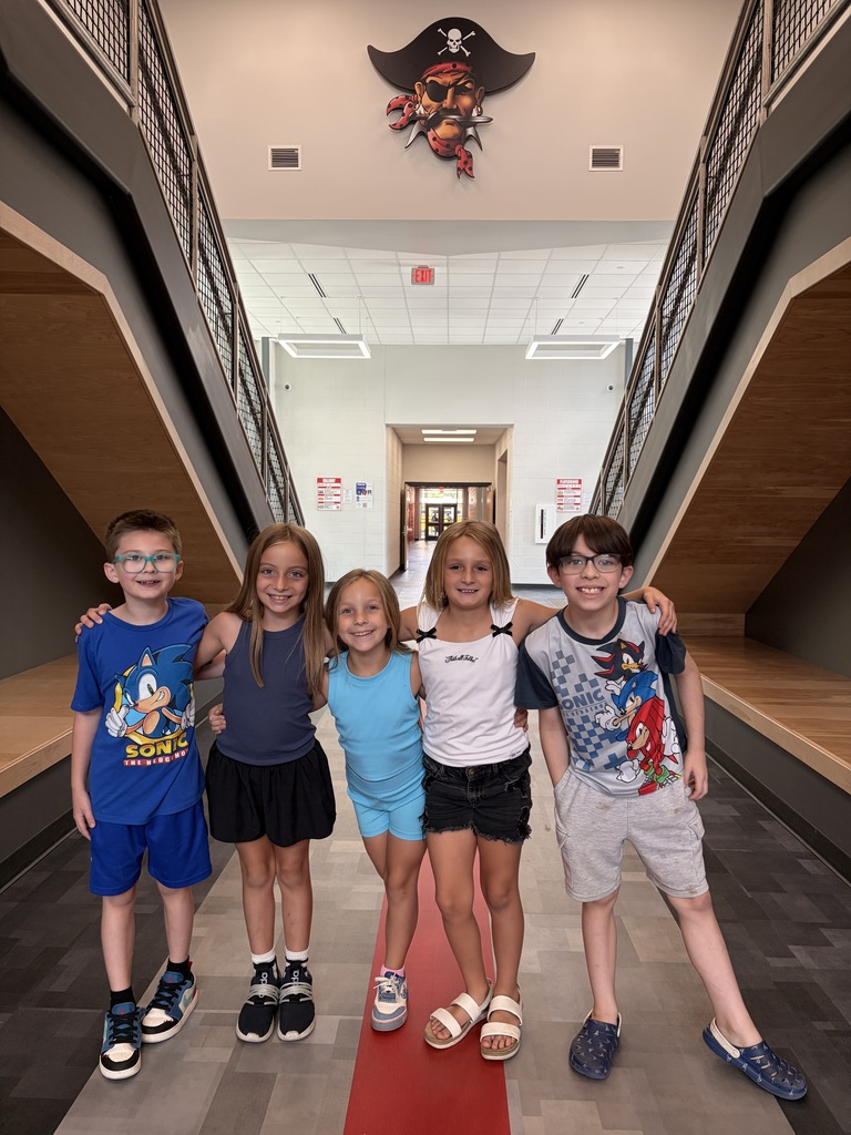 five students standing together in a hallway with a Pirate logo pictured in the background on the wall above them