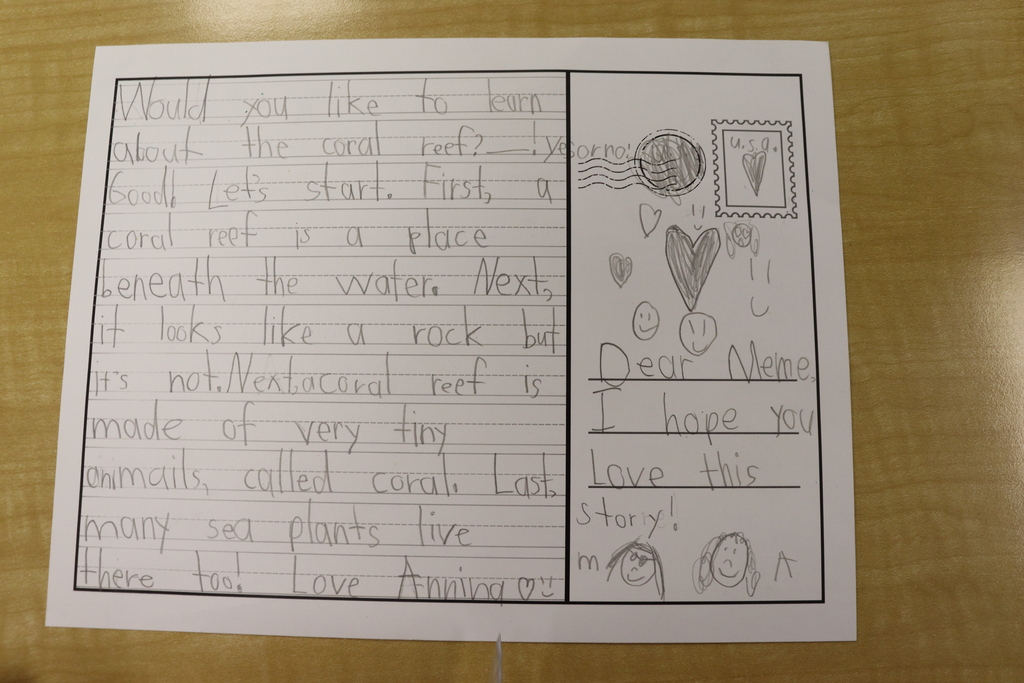 A handwritten letter is placed on a wooden surface. It drawings of a heart and a smiley face.