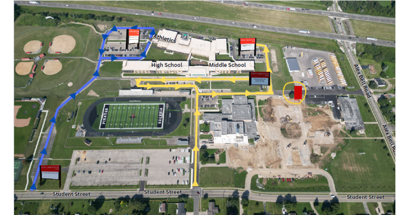aerial view of middle/high school with arrows indicating traffic flow. Parking lots and sports fields are visible.