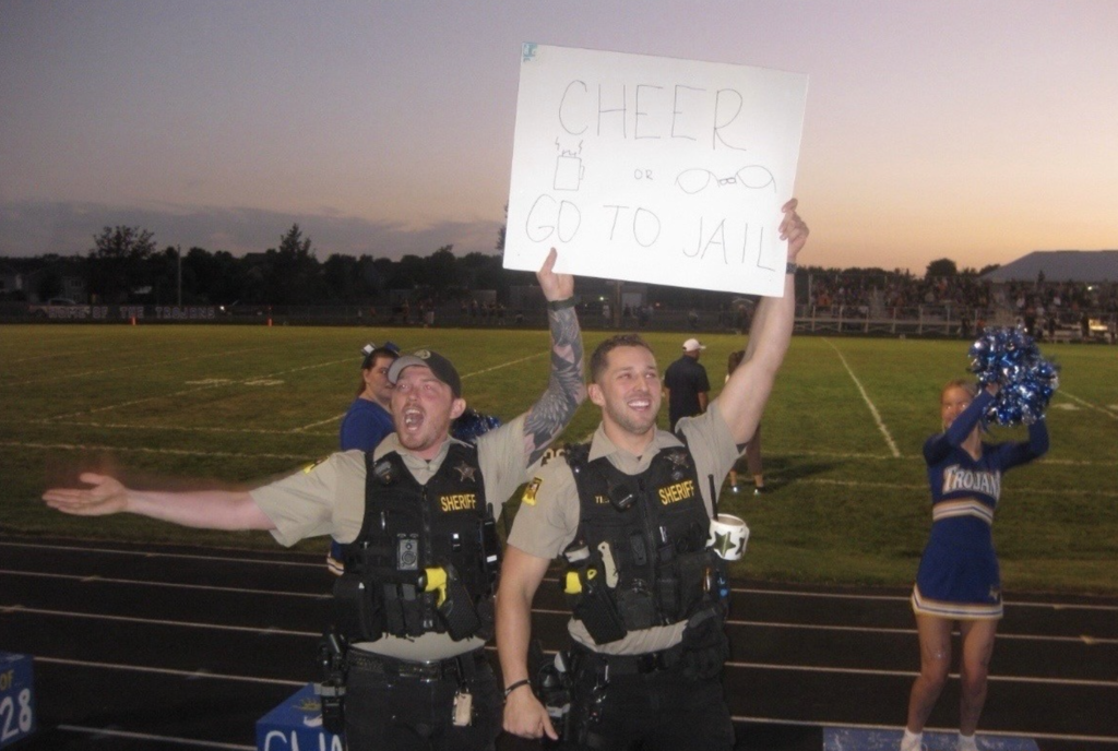 police holding a sign that says "cheer or go to jail"