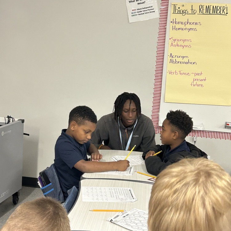 8th grade student helps elementary students with math lesson.