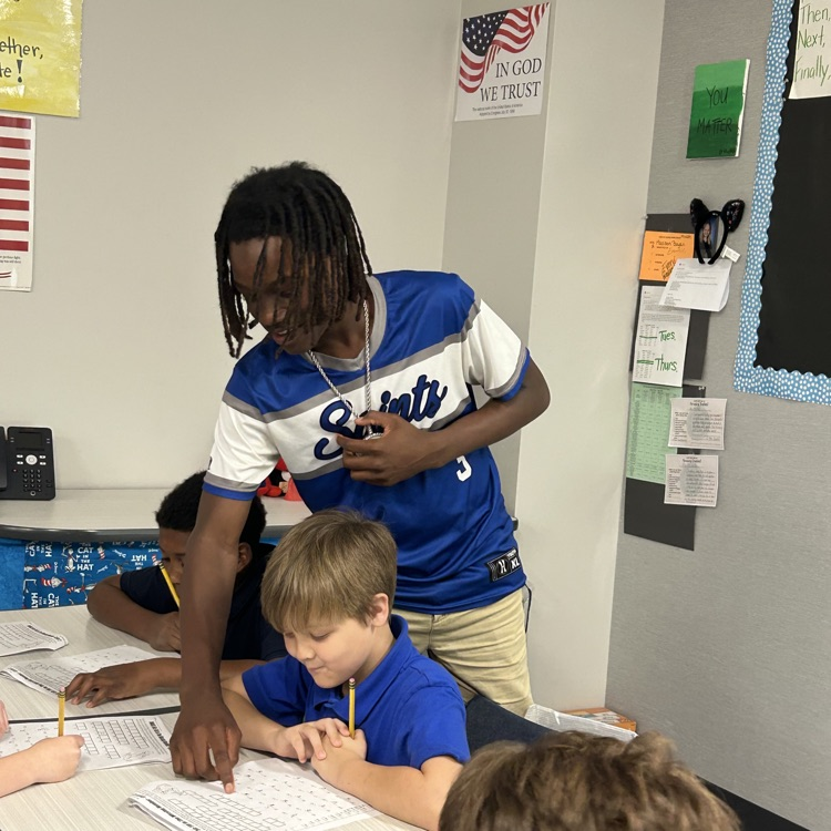 8th grade student helps elementary students with math lesson.