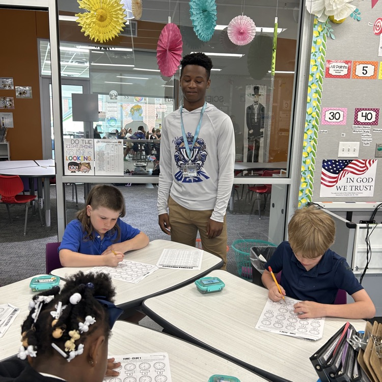 8th grade student helps elementary students with math lesson.