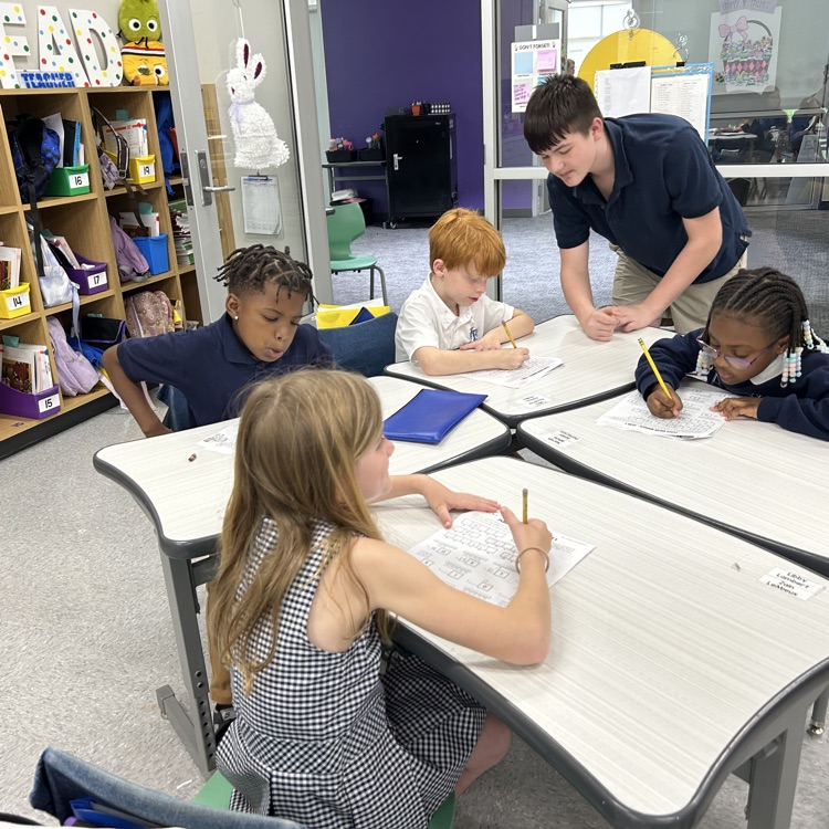 8th grade student helps elementary students with math lesson.