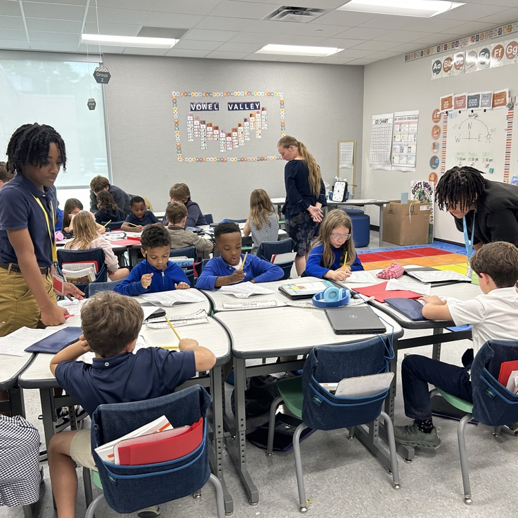 8th grade student helps elementary students with math lesson.