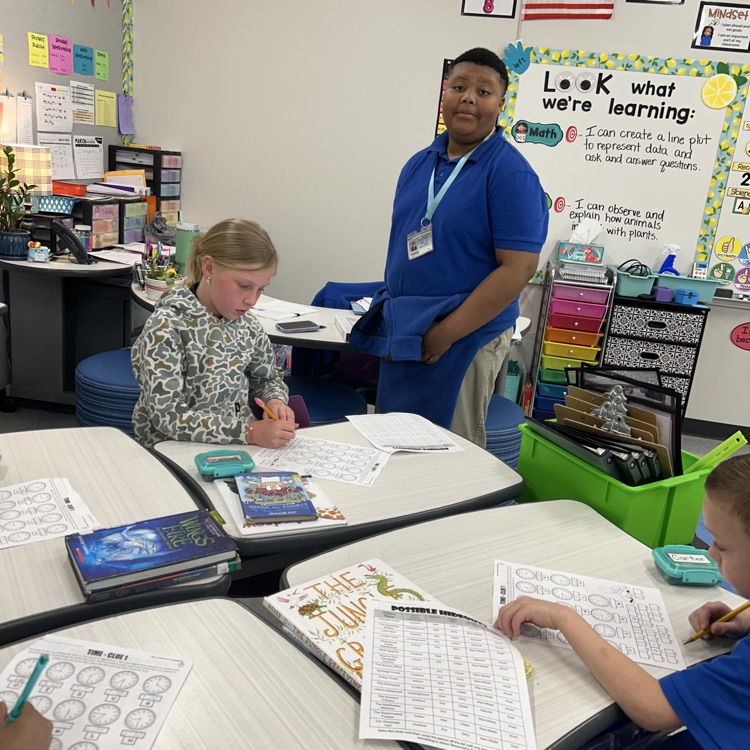 8th grade student helps elementary students with math lesson.