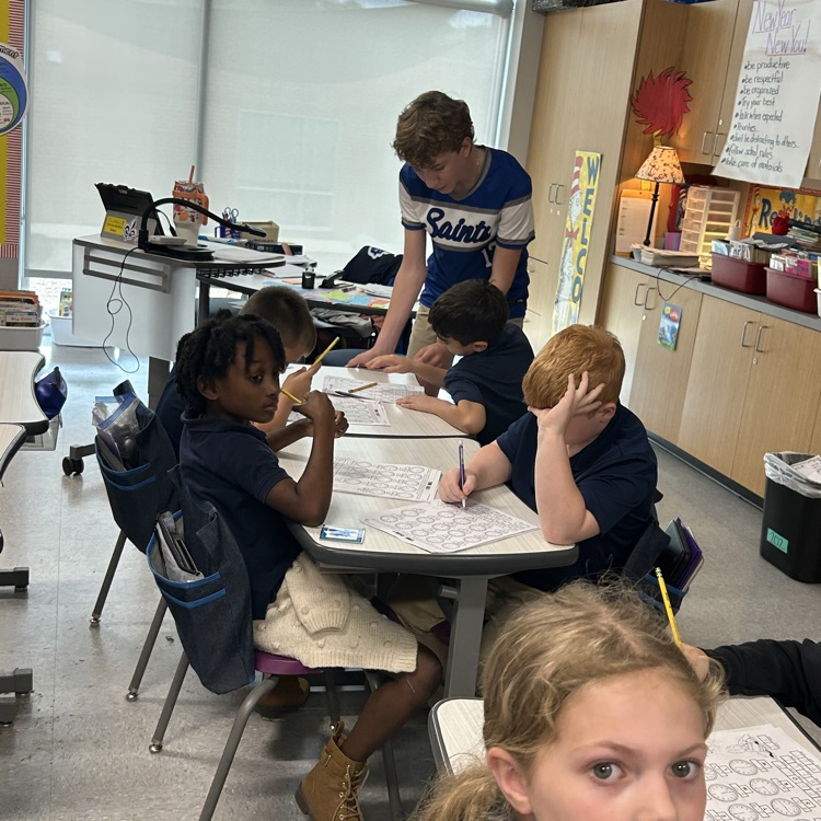 8th grade student helps elementary students with math lesson.