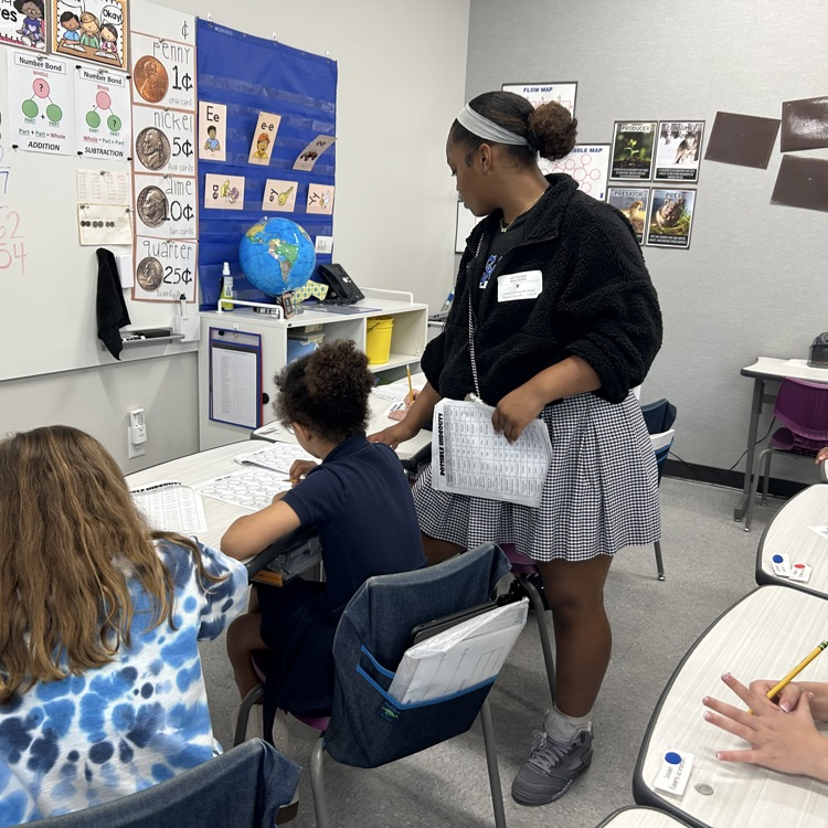 8th grade student helps elementary students with math lesson.