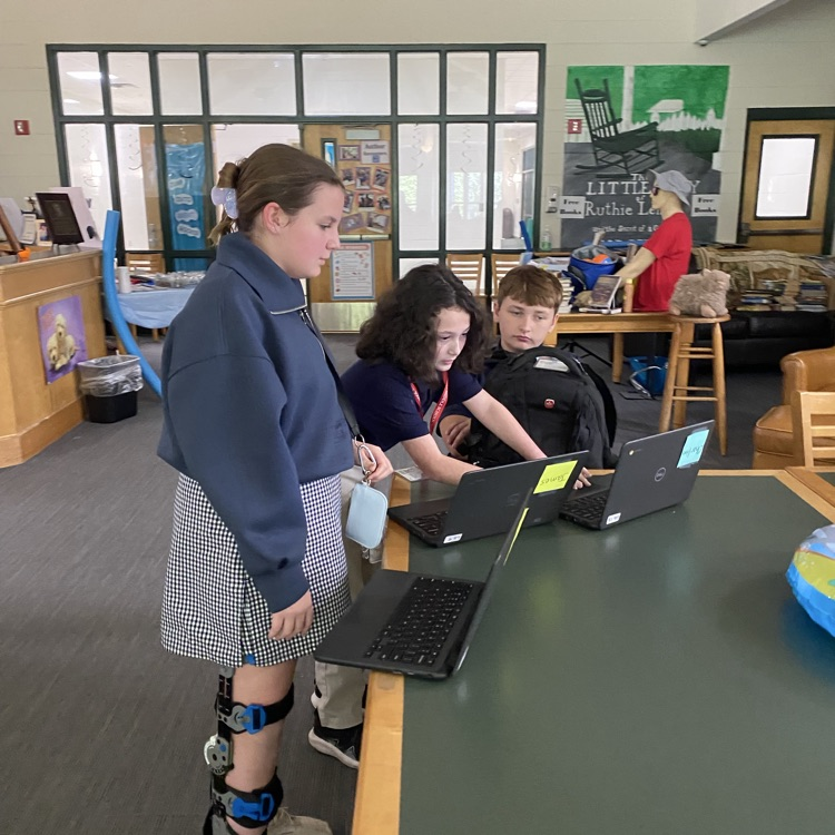 students picture collaborating around table with a computer