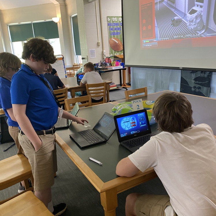 students picture collaborating around table with a computer