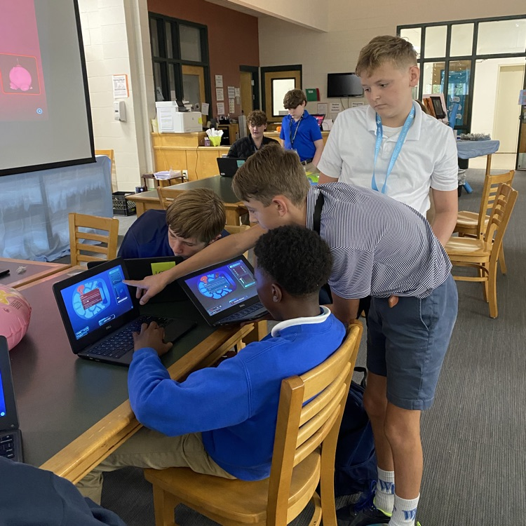 students picture collaborating around table with a computer