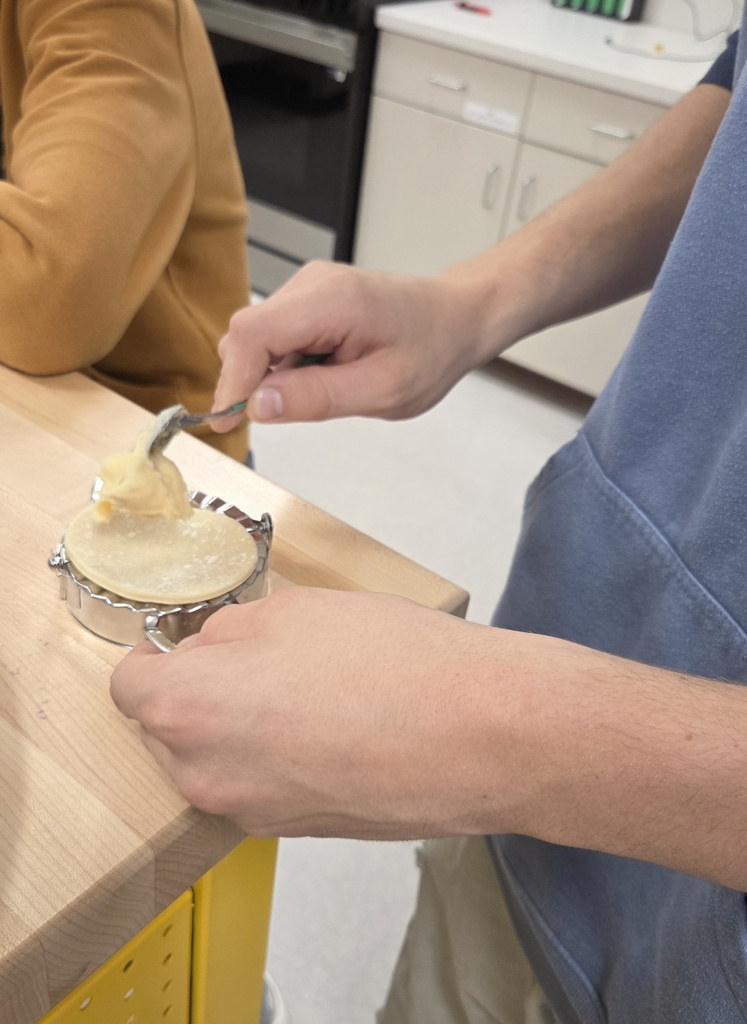 A student fills dough with a cheese and potato mixture.