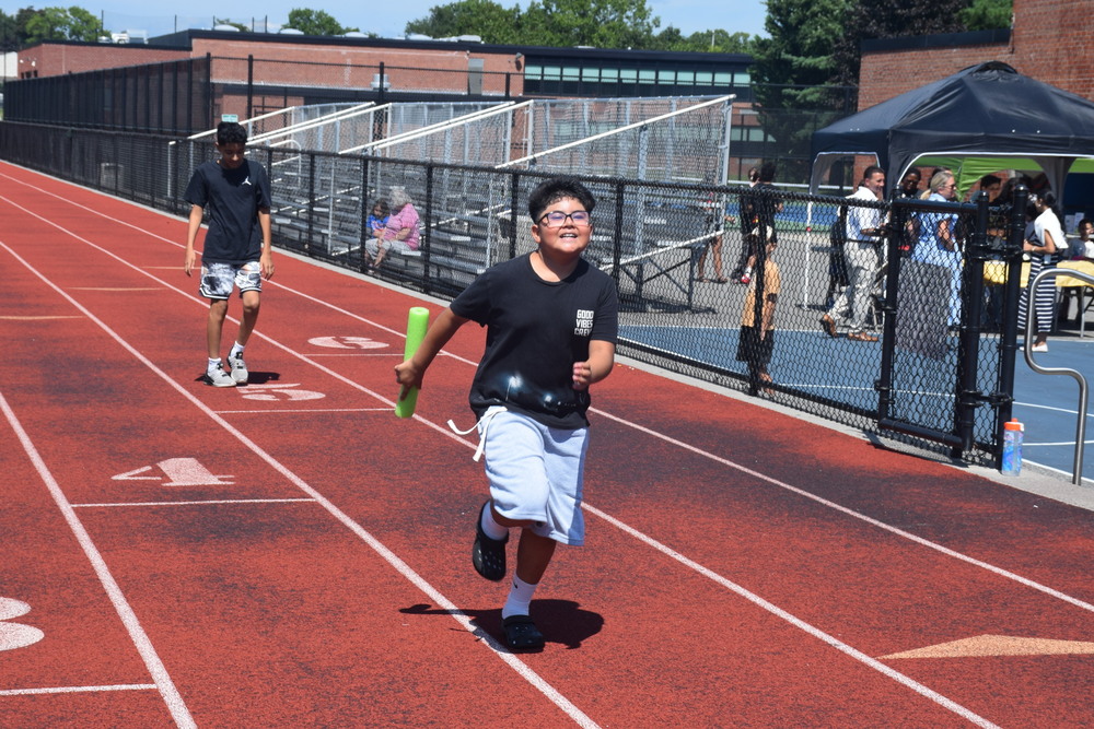Student running relay race on field.