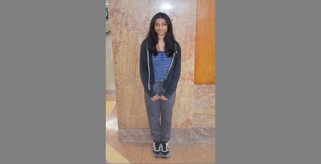 Young woman standing in a casual outfit of a striped shirt, hoodie, and sweatpants against a textured wall, perfect for a lifestyle or fashion blog.