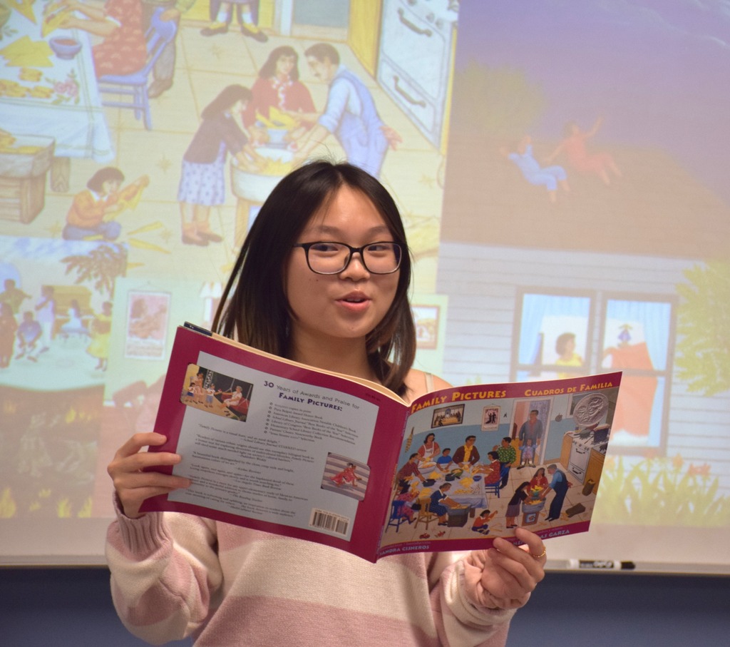 Photo of high school student reading a book to younger students.