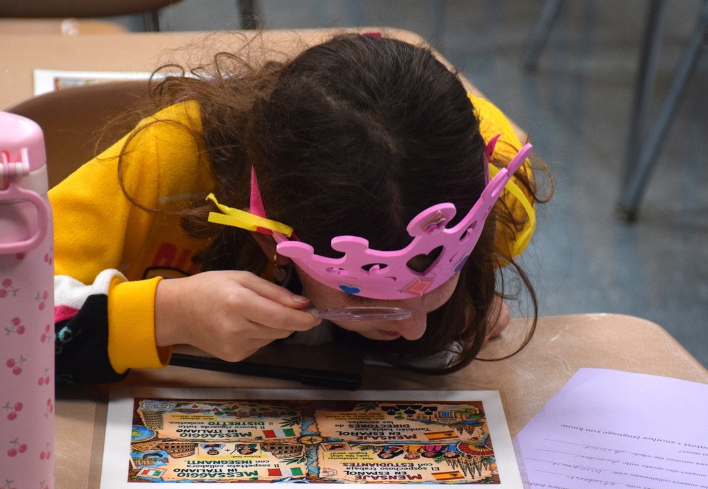 Photo of student sitting at desk and using a magnifying glass.
