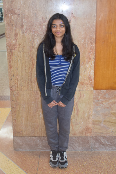 Young woman standing in a casual outfit of a striped shirt, hoodie, and sweatpants against a textured wall, perfect for a lifestyle or fashion blog.