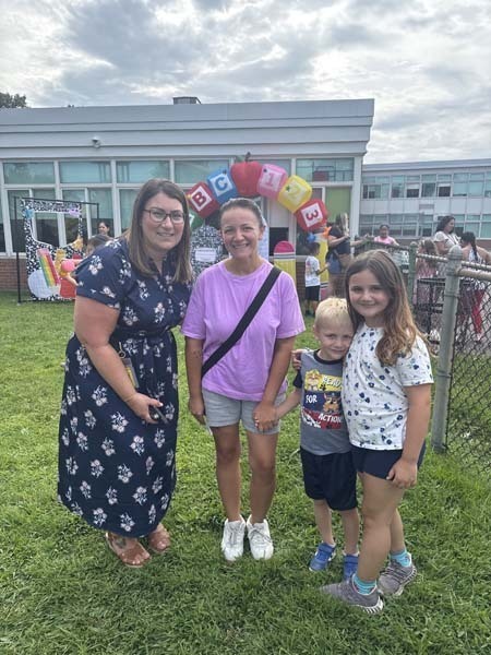 Two students smiling with adult outside at fair.