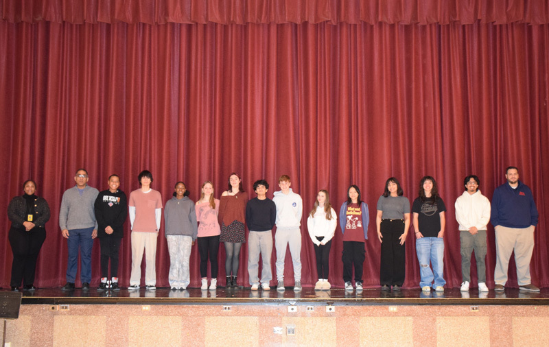 people stand in a line on a stage with red curtains. They appear confident and composed, suggesting a formal or celebratory event.
