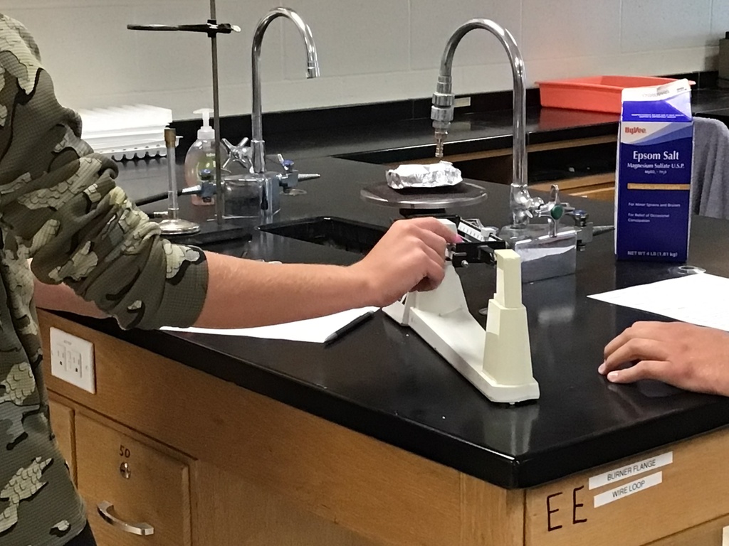 Student adjusting a triple beam balance to find the mass of a heated sample.