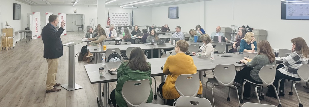 people in large room with presenter int he front 