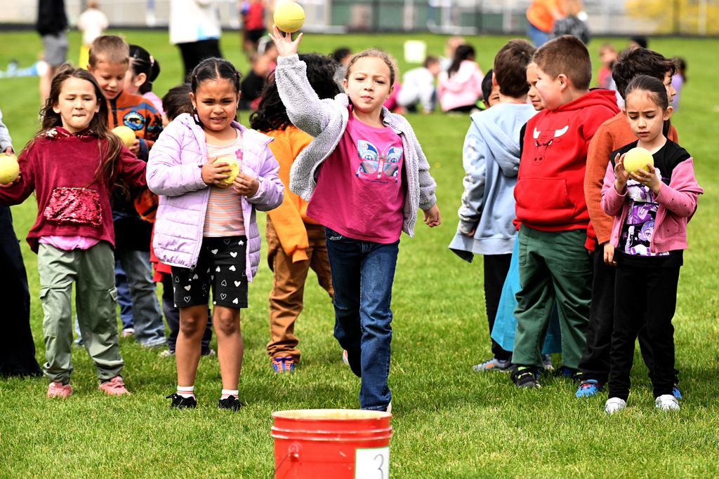 a girl throwing a ball at a bucket with her friends in the background.