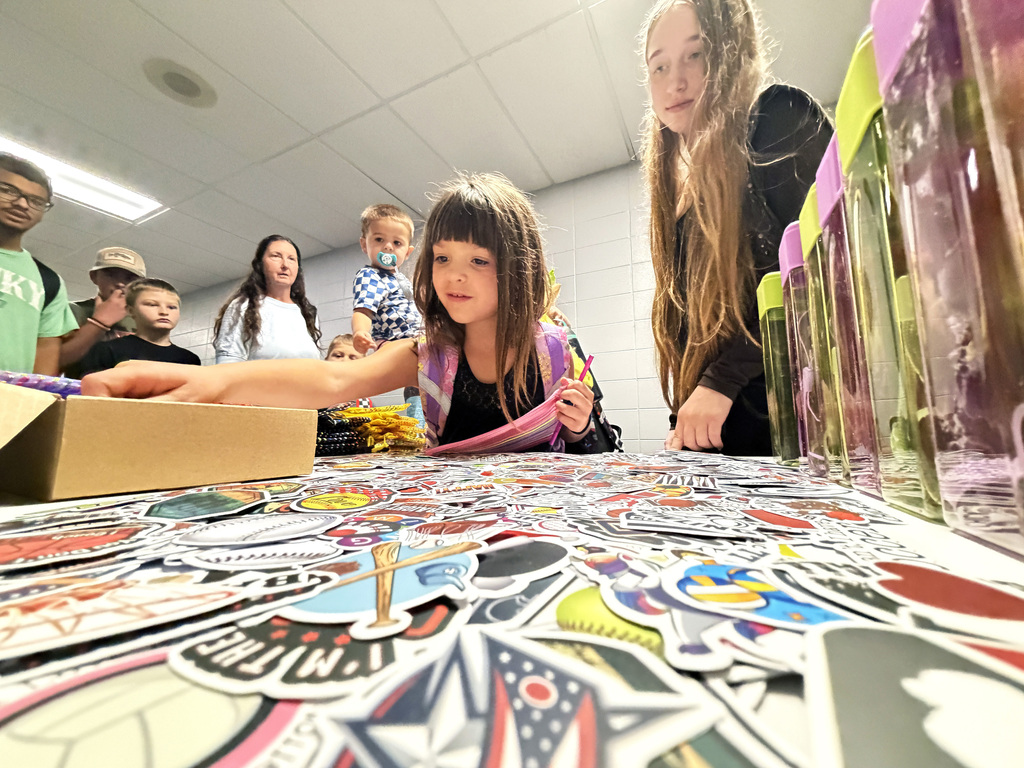 two girls looking at stickers on a table, one reaching into a box