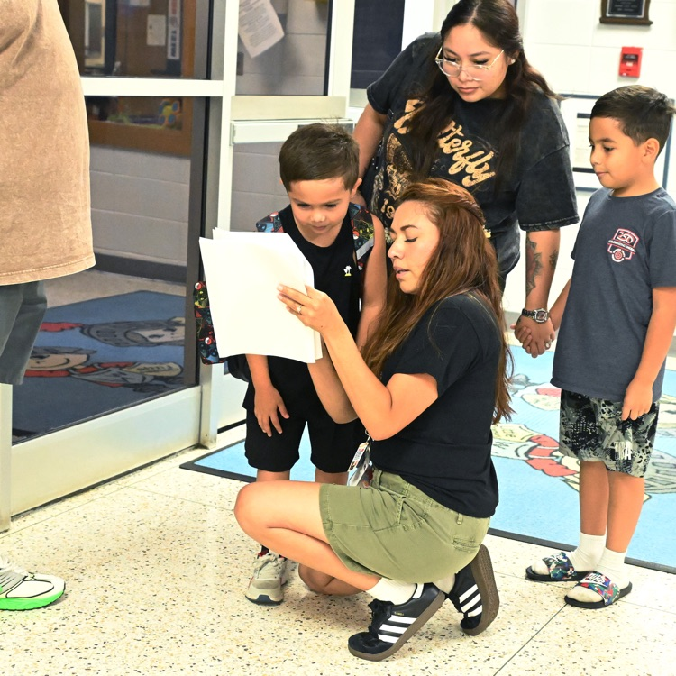 a teacher kneeling with a student looking at a paper