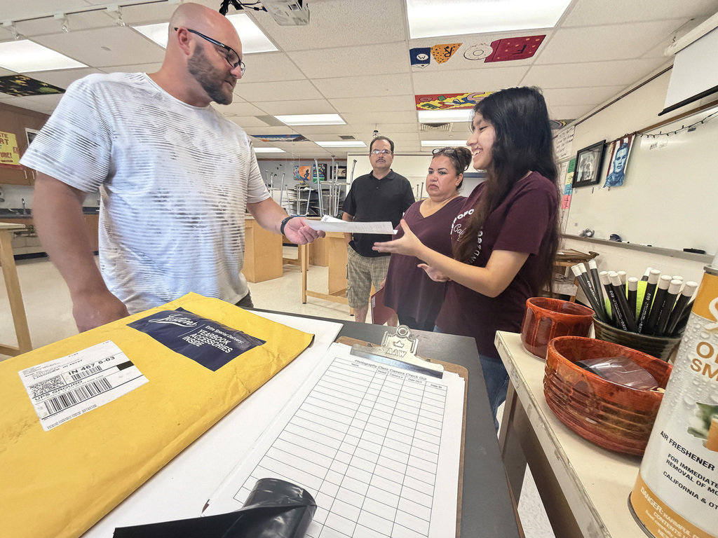 a teacher handing a paper to a student with two parents in the background